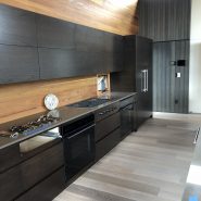 Select grade wood flooring shown in modern kitchen with black cabinets and appliances