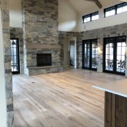Wide plank white oak flooring in living room with stone fireplace
